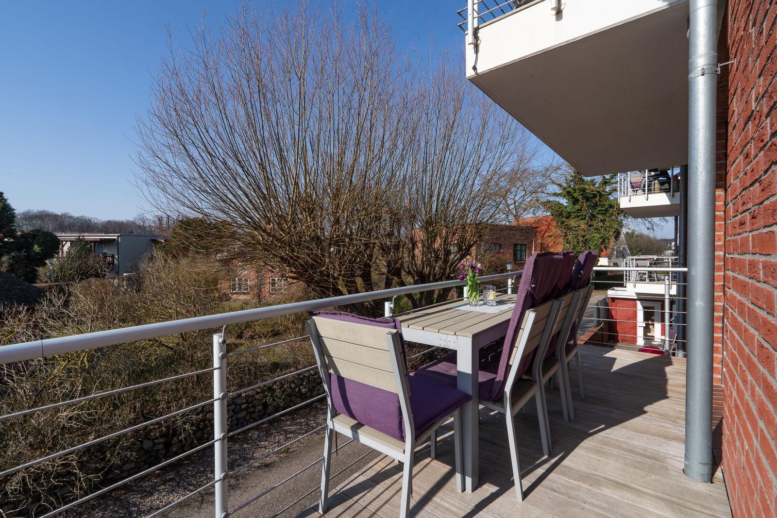 Terrasse mit Tisch und Stühlen, Blick auf Bäume und Gebäude.