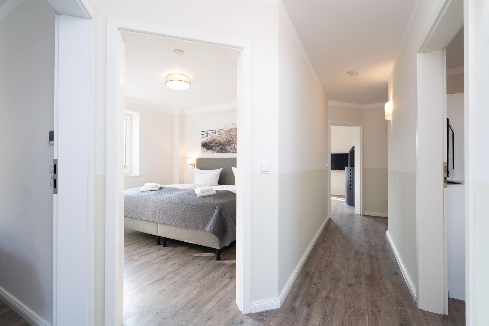 Schlafzimmer mit Bett und Wandbild. Flur mit Holzboden und Türen zu weiteren Räumen.
