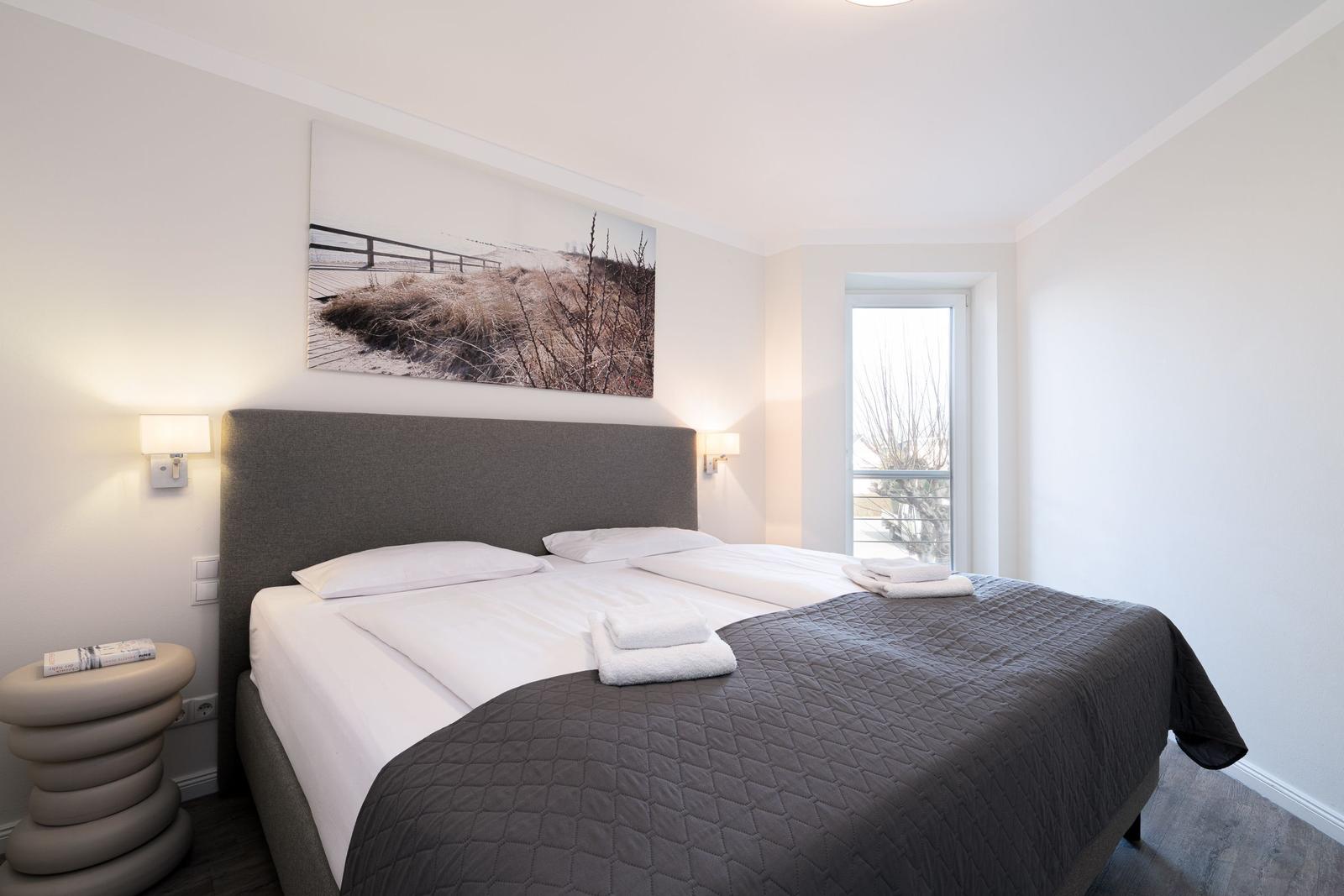 Schlafzimmer mit Doppelbett, Wandbild und Fenster zum Balkon.