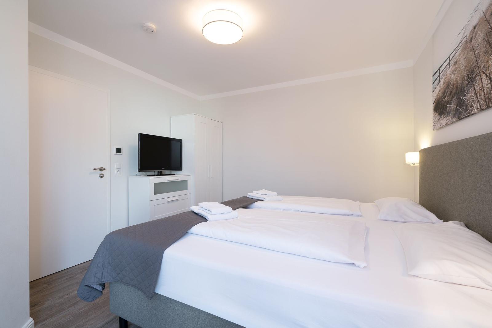 Schlafzimmer mit Doppelbett, Fernseher und Kleiderschrank.