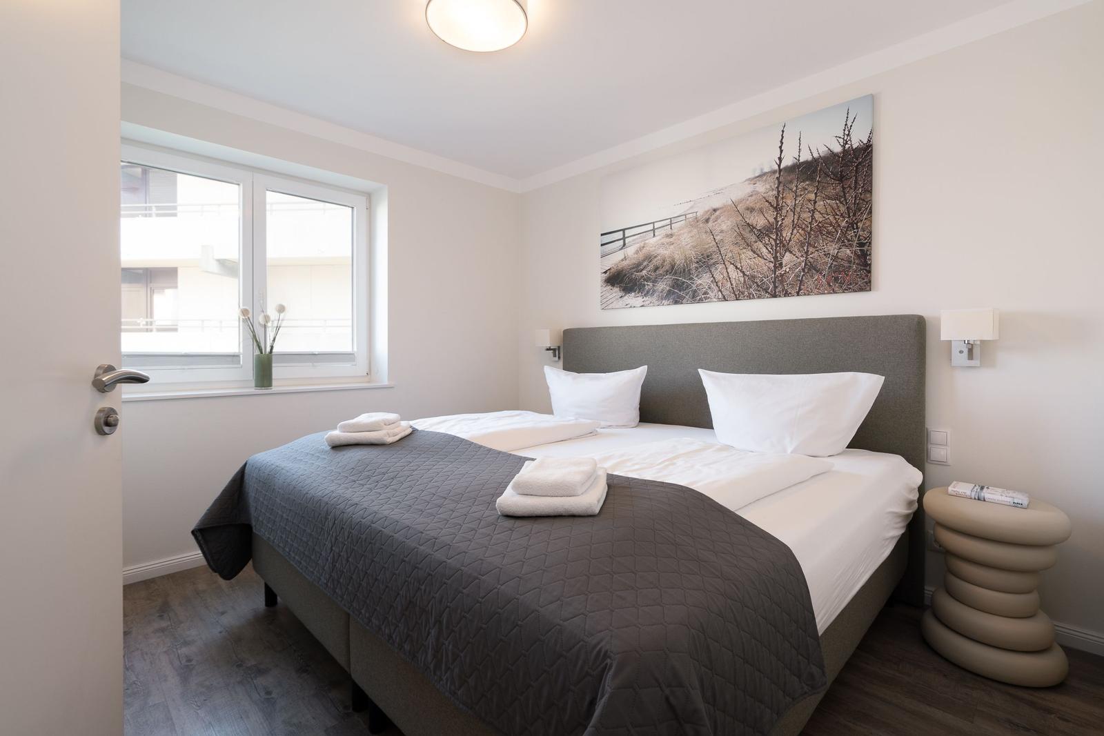 Schlafzimmer mit Doppelbett, Fenster und Wandbild.