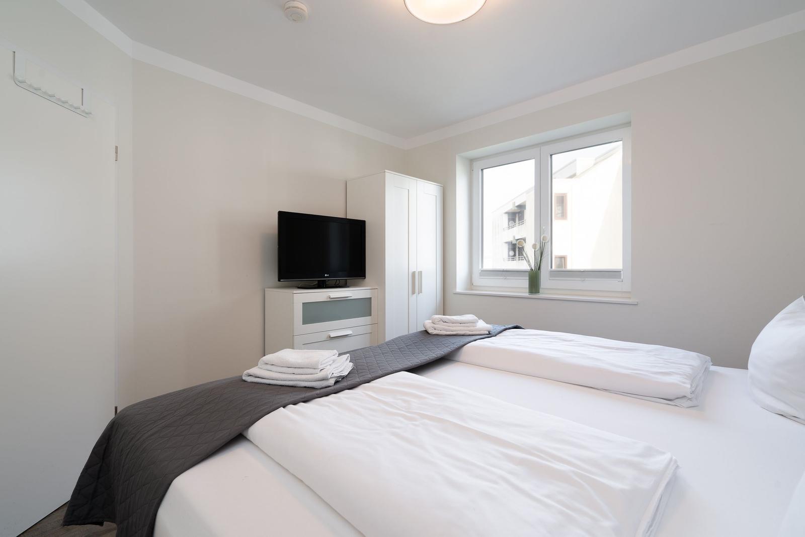 Schlafzimmer mit Doppelbett, TV und Fenster. Handtücher auf dem Bett.