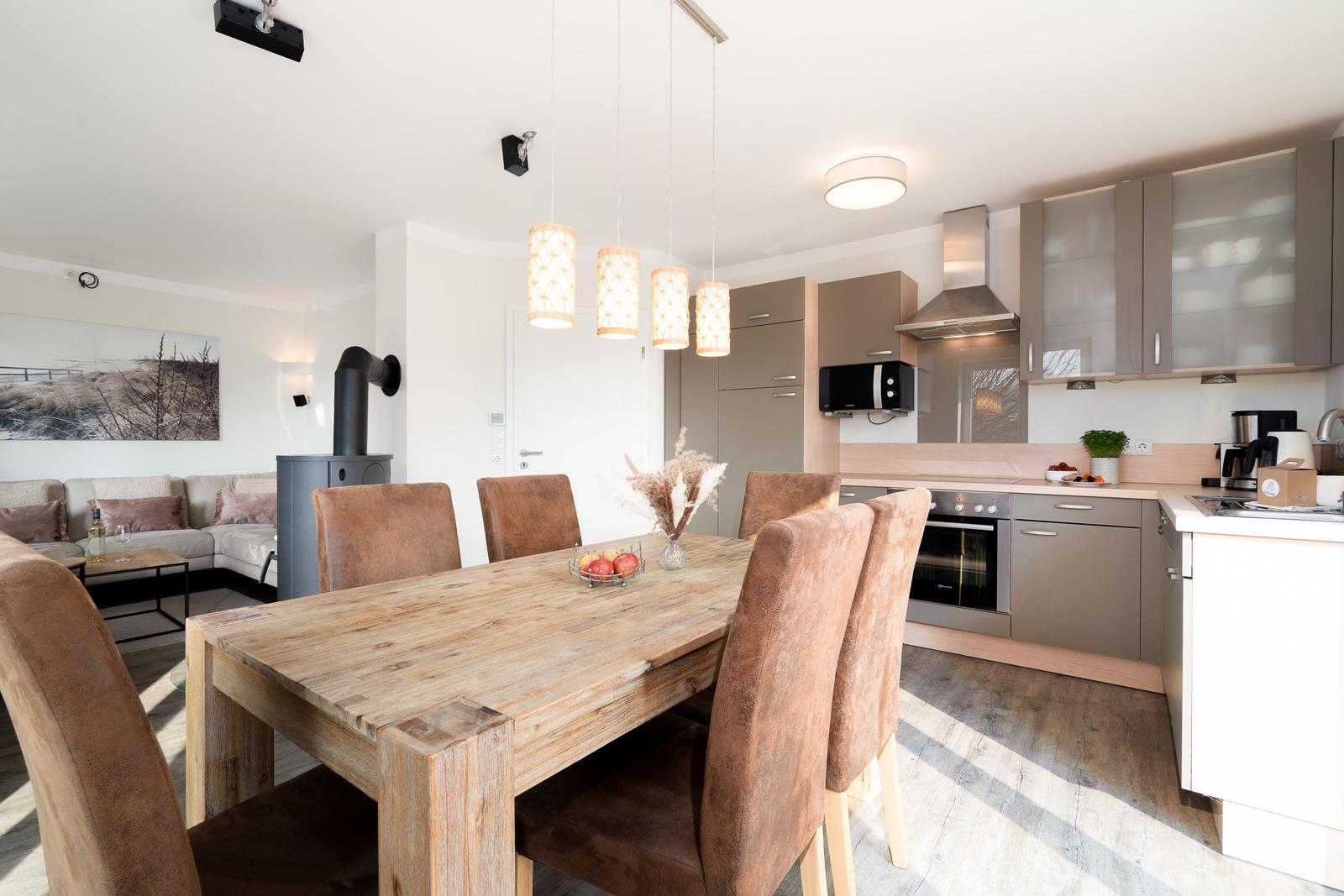 Essbereich mit Holztisch und Stühlen, Küche mit Geräten und Wohnbereich mit Sofa.