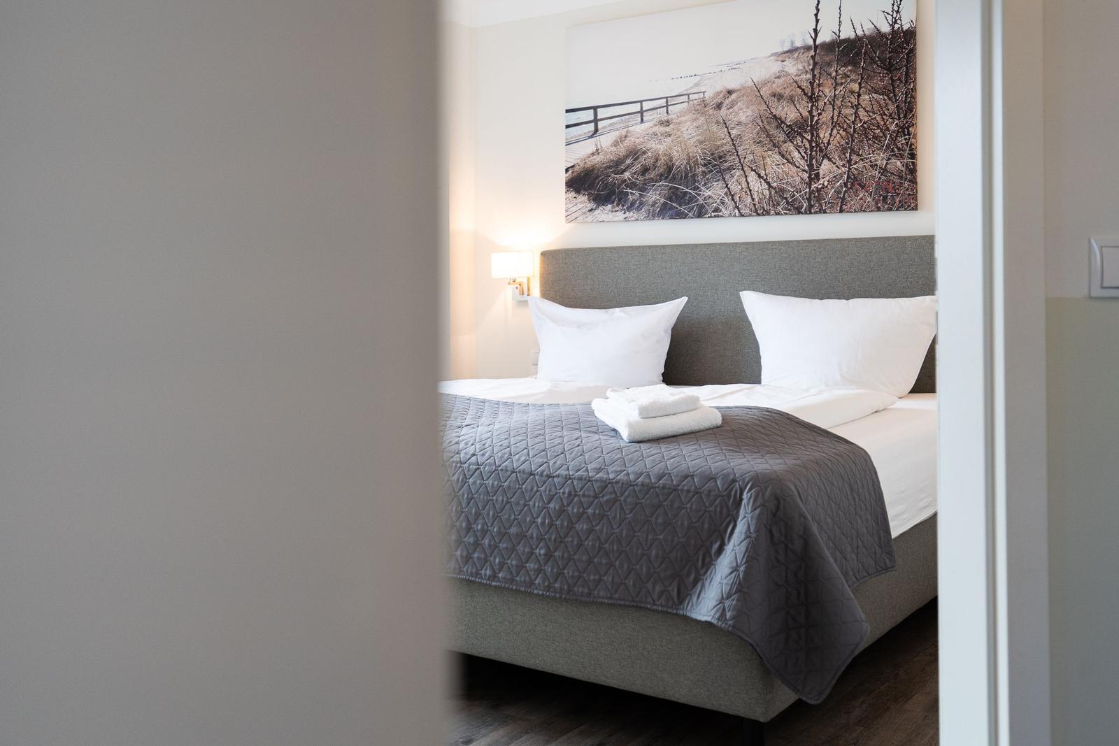 Schlafzimmer mit Bett, Kopfkissen und Wandbild.