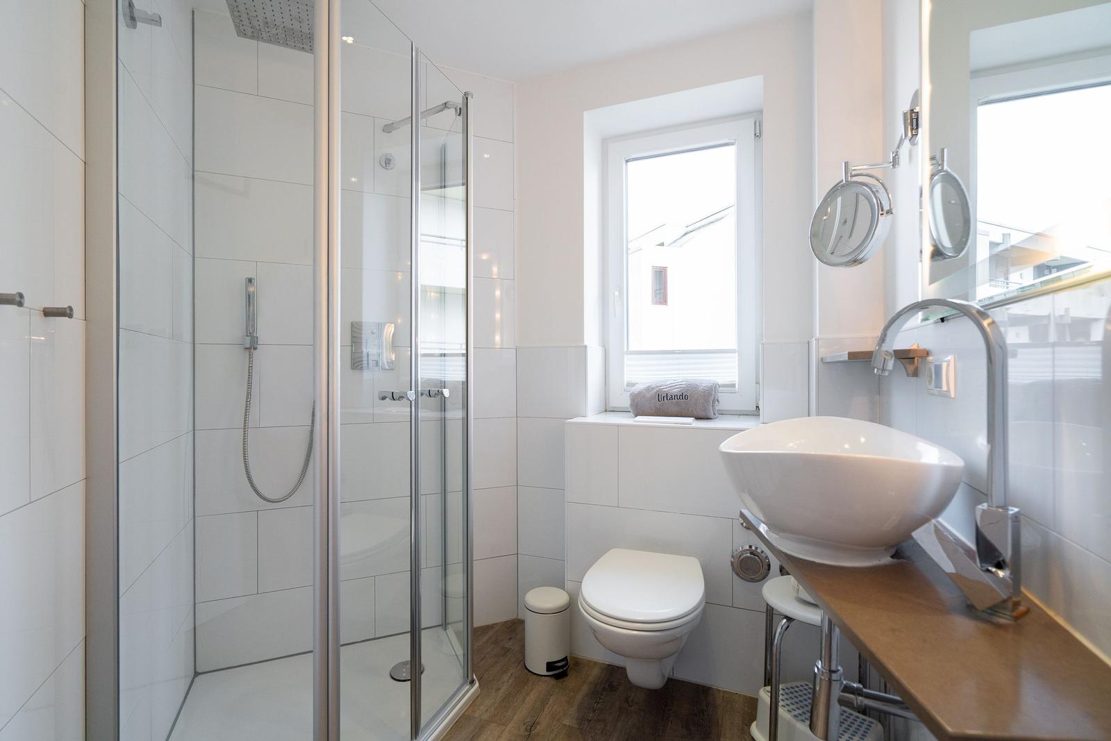 Badezimmer mit Dusche, Waschbecken und Toilette. Fenster sorgt für Tageslicht.