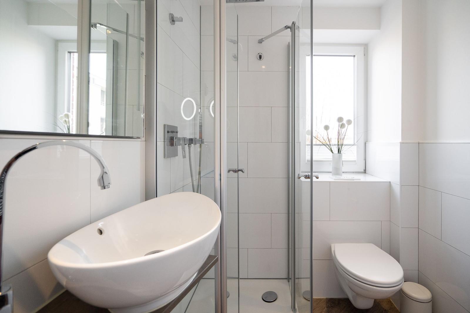 Badezimmer mit Dusche, Waschbecken und WC. Fenster mit Pflanze.