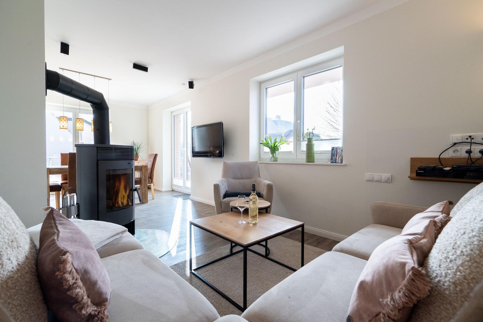 Wohnzimmer mit Kamin, Sofa, Couchtisch und Fernseher. Fenster mit Blick auf Außenbereich.
