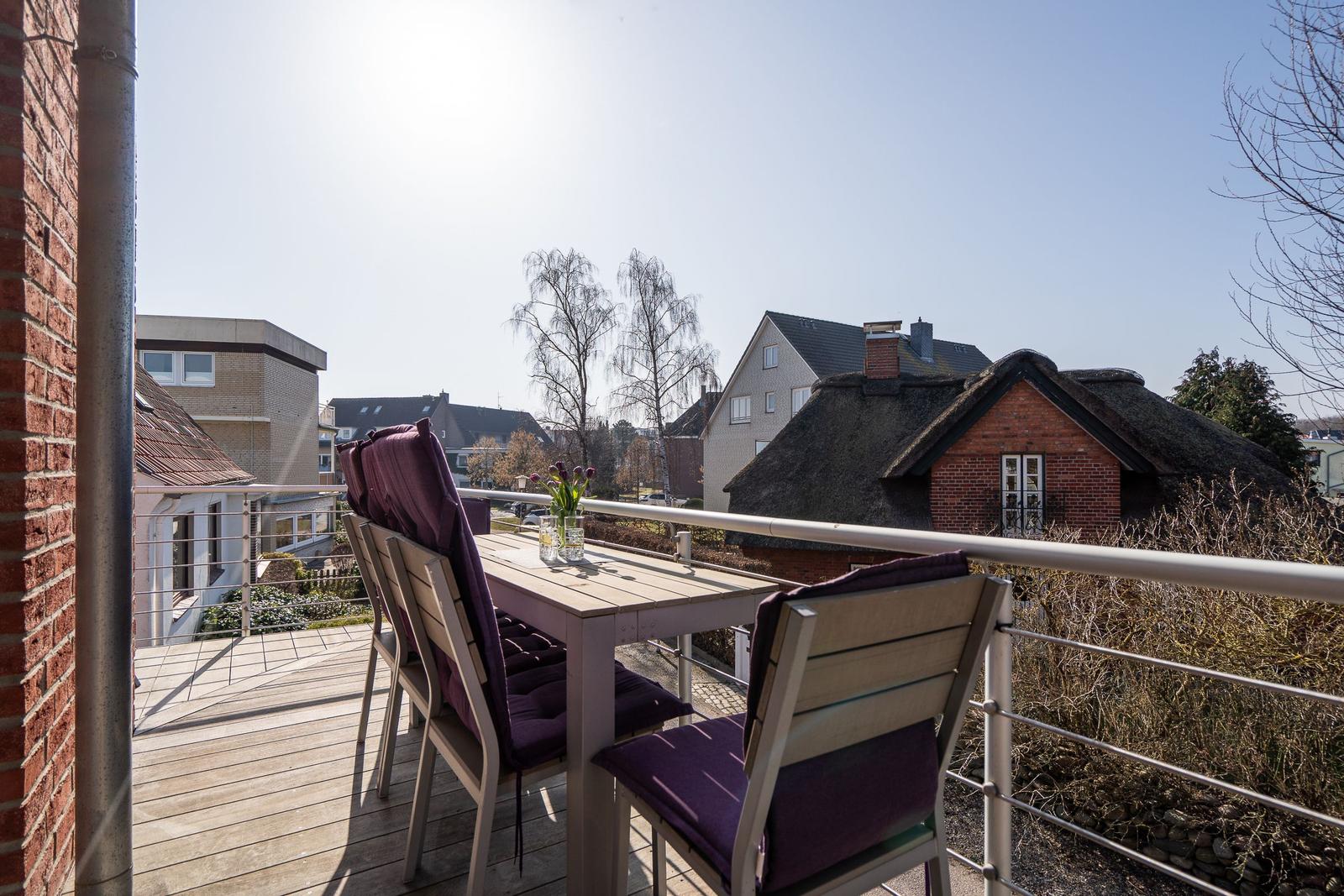 Terrasse mit Tisch und Stühlen, Blick auf Dächer und Bäume.