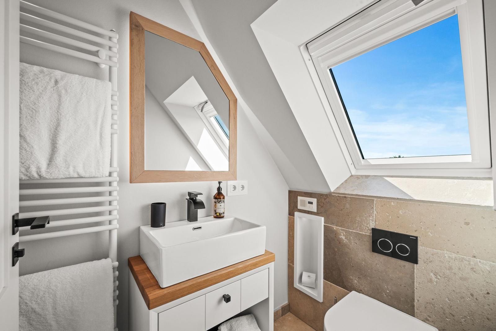 Badezimmer mit Dachschrägen, Waschbecken, Spiegel und Dachfenster.