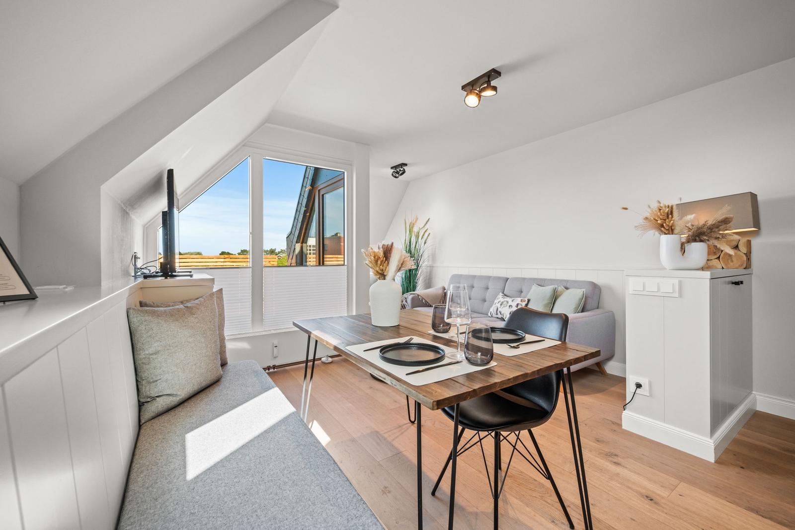 Essbereich mit Tisch, Stühlen und Sofa. Fenster mit Blick auf Außenbereich.