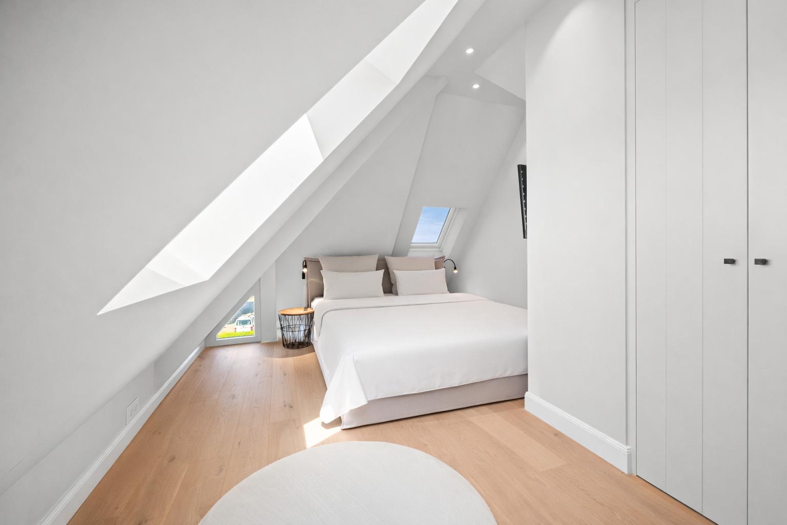 Schlafzimmer mit Dachschrägen, weißem Bett und Holzboden