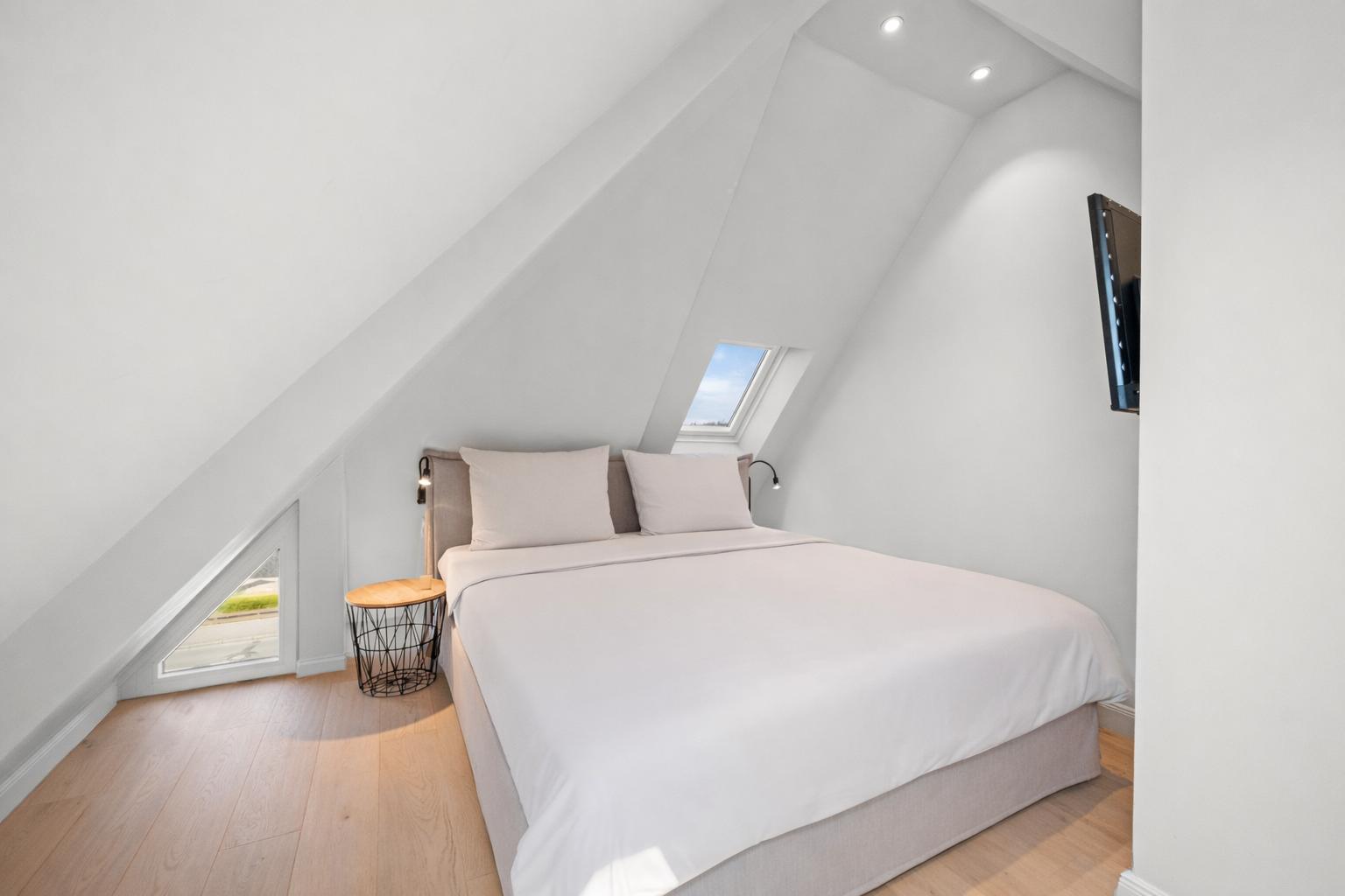 Schlafzimmer mit Dachschrägen, Bett, Fenster und Fernseher.
