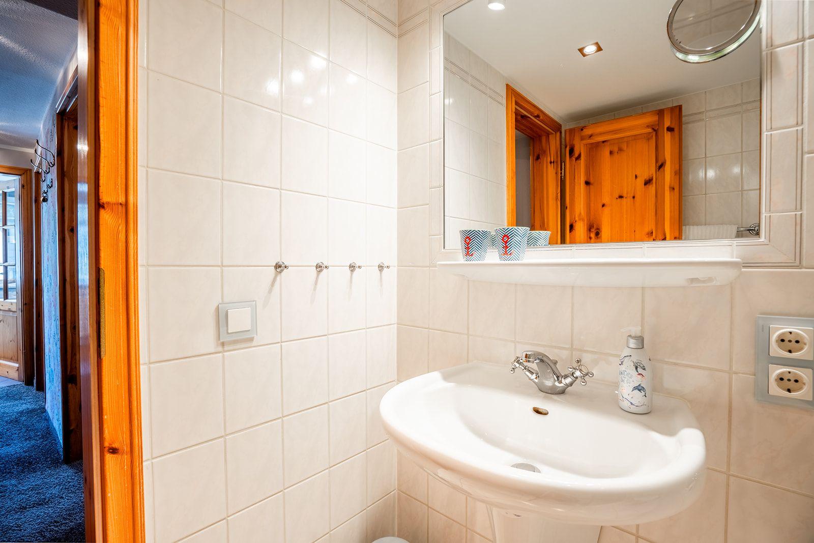 Badezimmer mit Waschbecken, Spiegel und Holztür