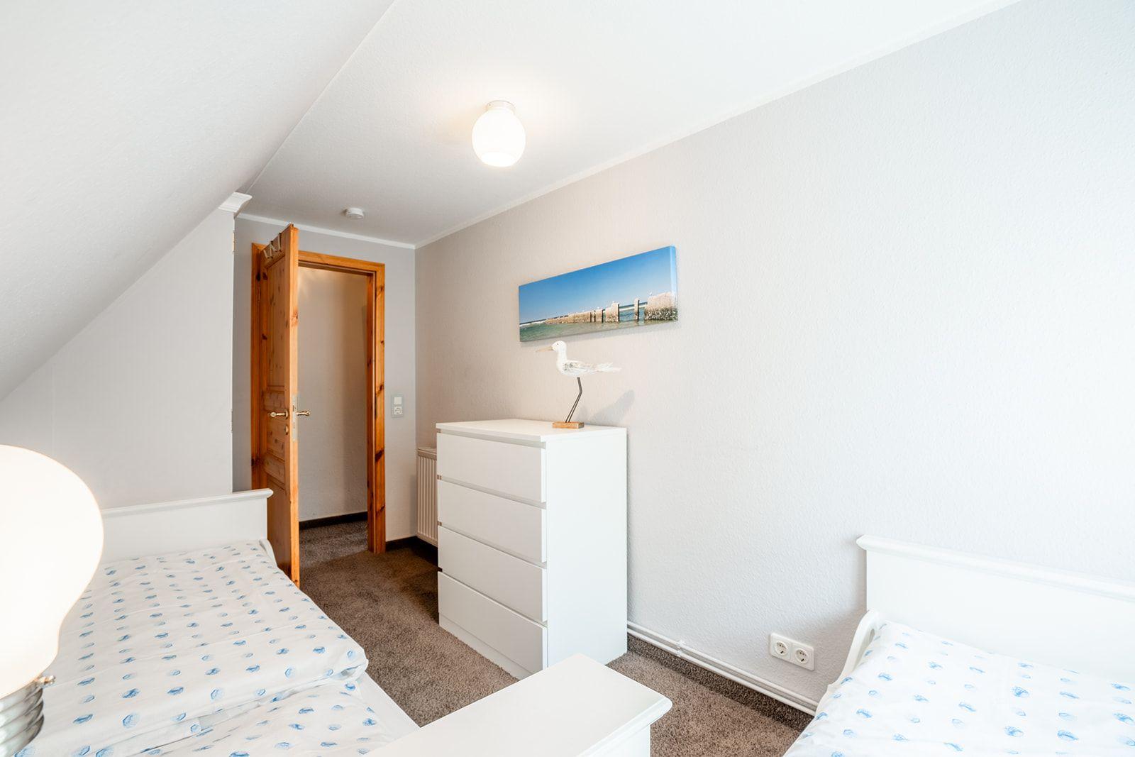 Zwei Betten, weißer Schrank, Wandbild und Tür im Dachgeschosszimmer.