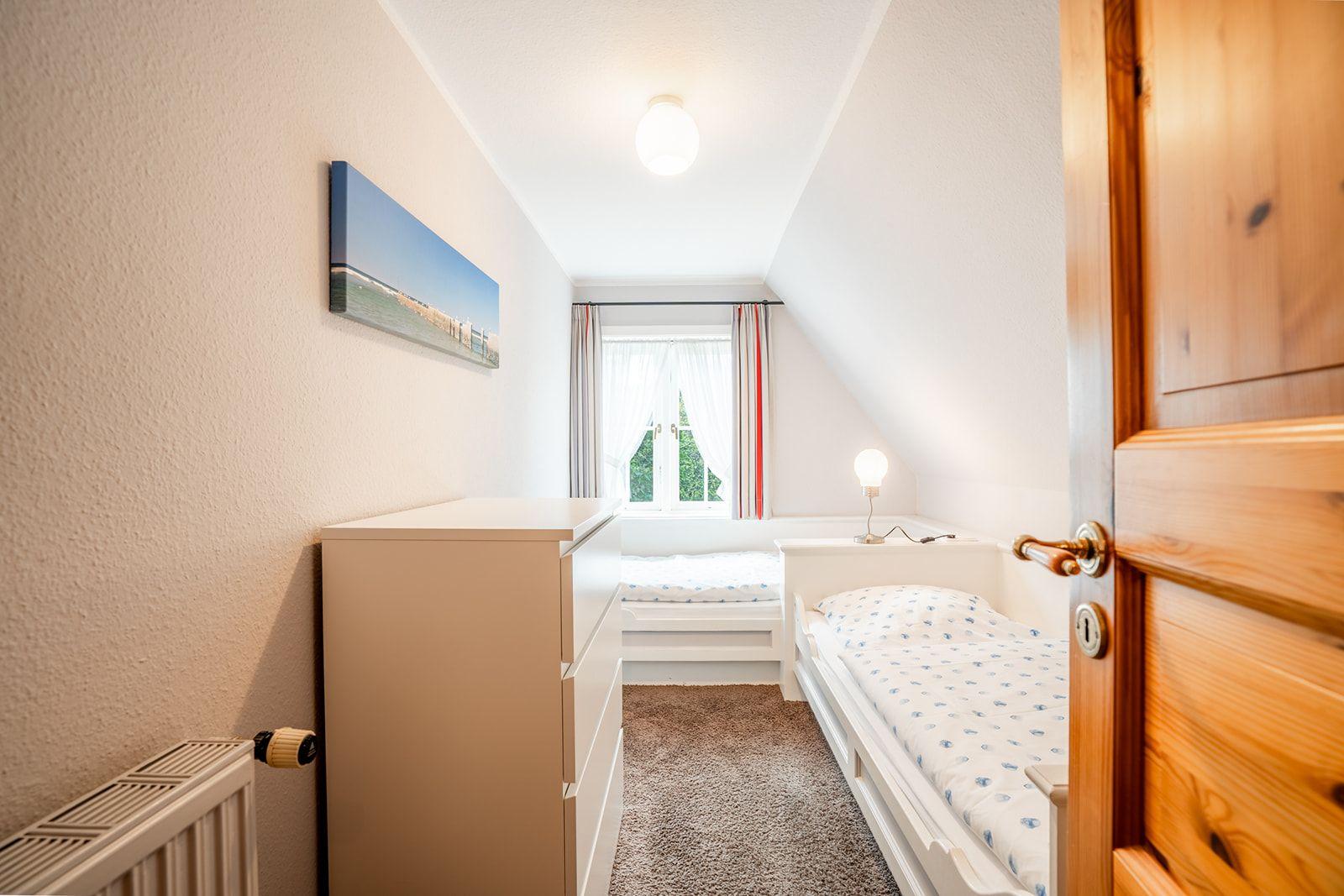 Schlafzimmer mit Dachschräge, zwei Betten und Fenster mit Vorhängen.