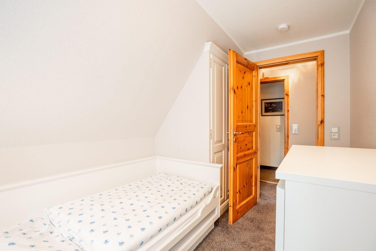Schlafzimmer mit Einzelbett, Holztür und weißen Möbeln.