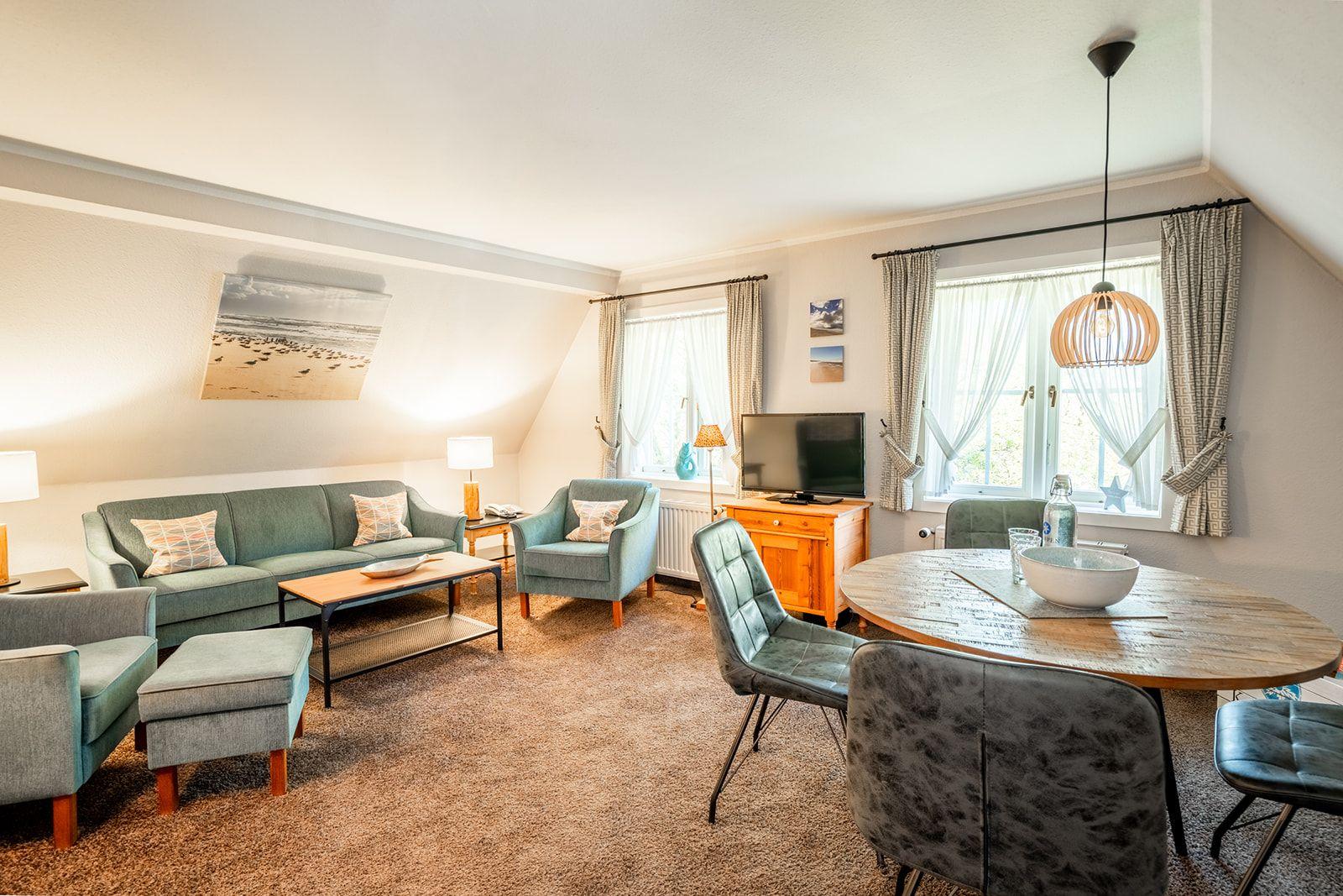 Wohn- und Essbereich mit Sofa, Stühlen und Tisch. Fenster mit Vorhängen und Deckenlampe.