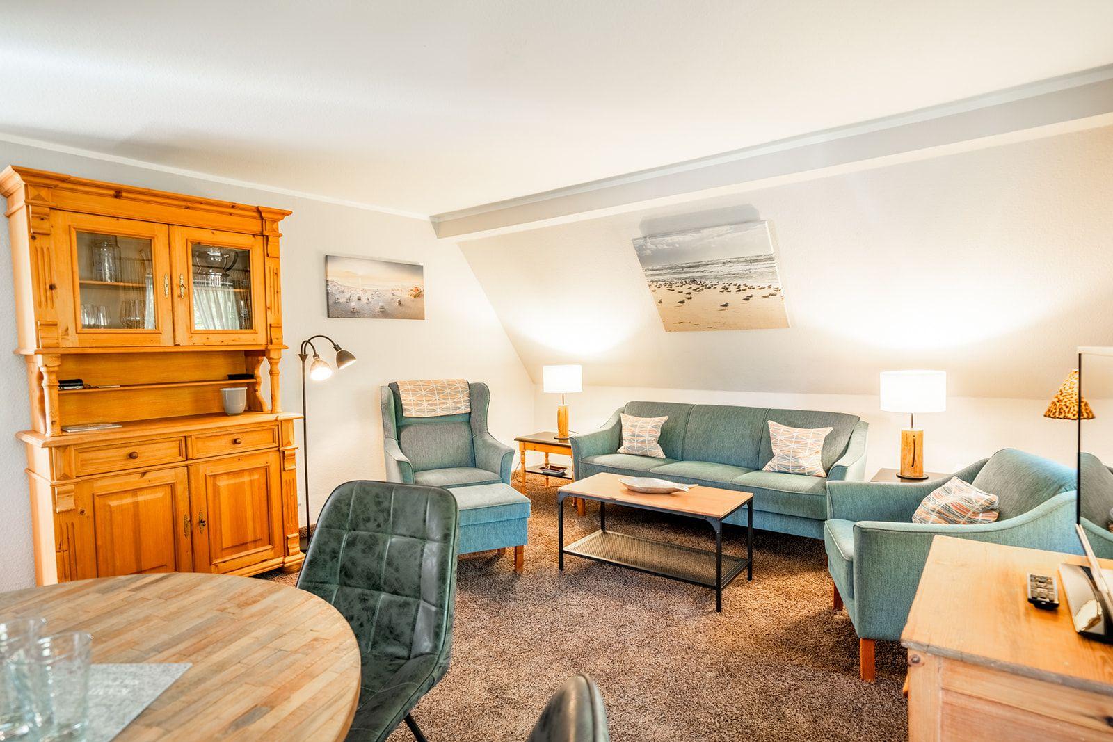 Wohnzimmer mit Sofa, Sesseln und Holzmöbeln unter Dachschrägen.