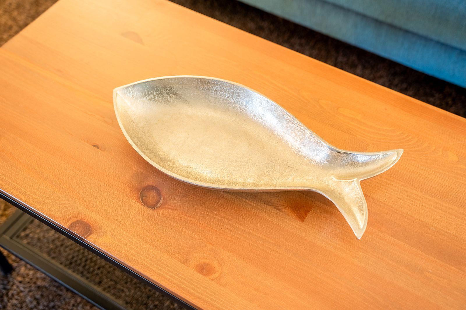 Ein silbernes Fischschale-Objekt auf einem Holztisch.