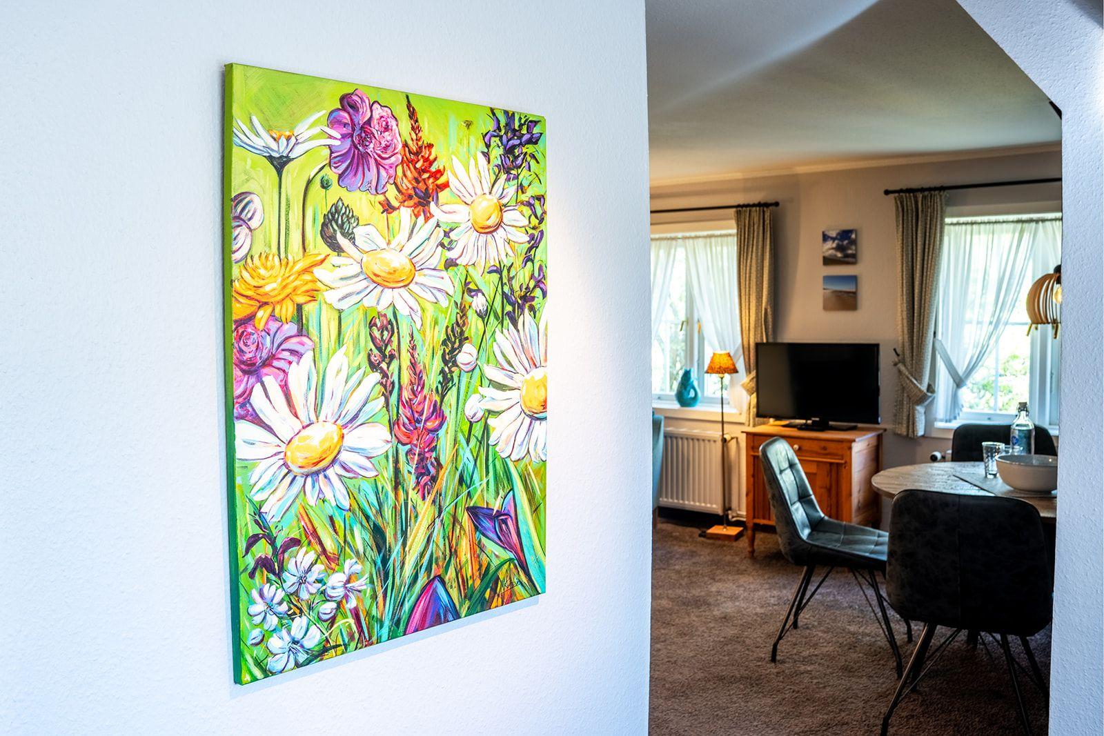Ein großes Wandbild mit Blumen hängt in einem Wohnbereich mit Essplatz und TV.