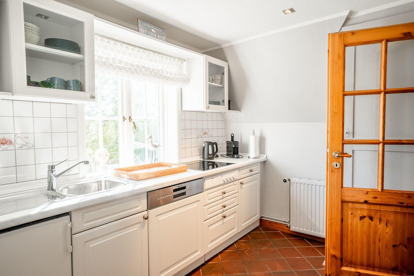 Küche mit weißen Schränken, Fenster und Holztür.
