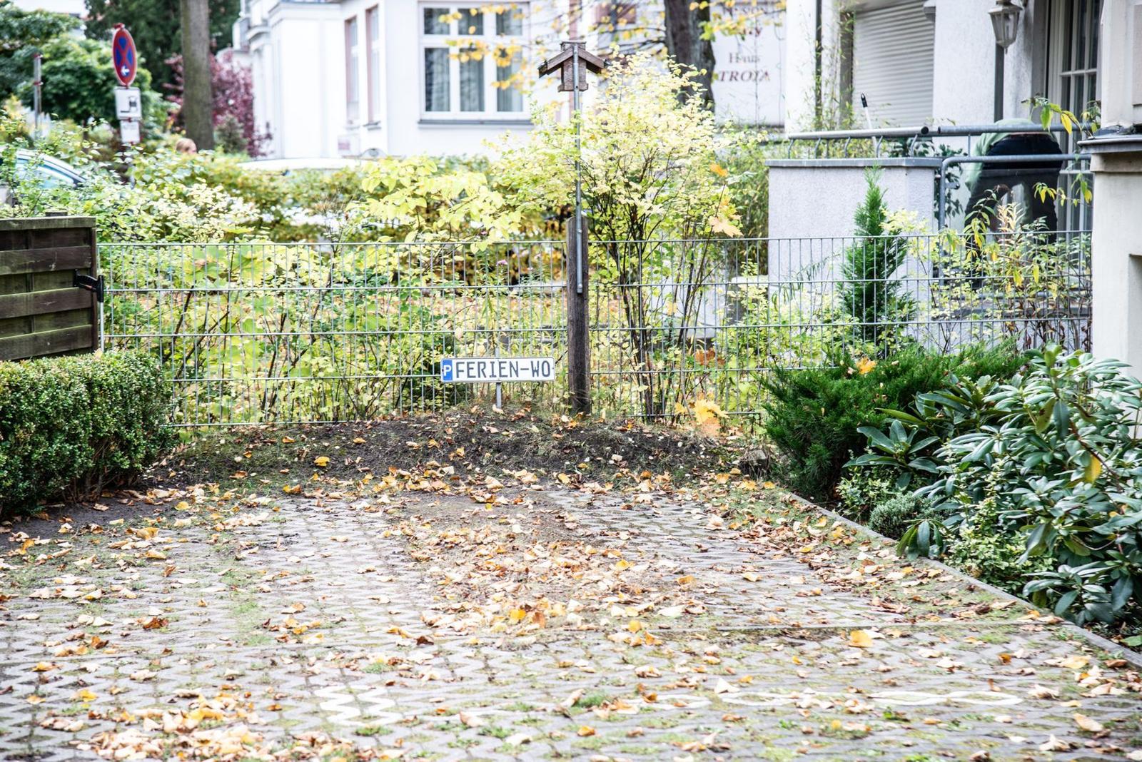 Pfadschild mit P FERIEN-WO an Zaun. Blätter bedecken den Kiesweg.