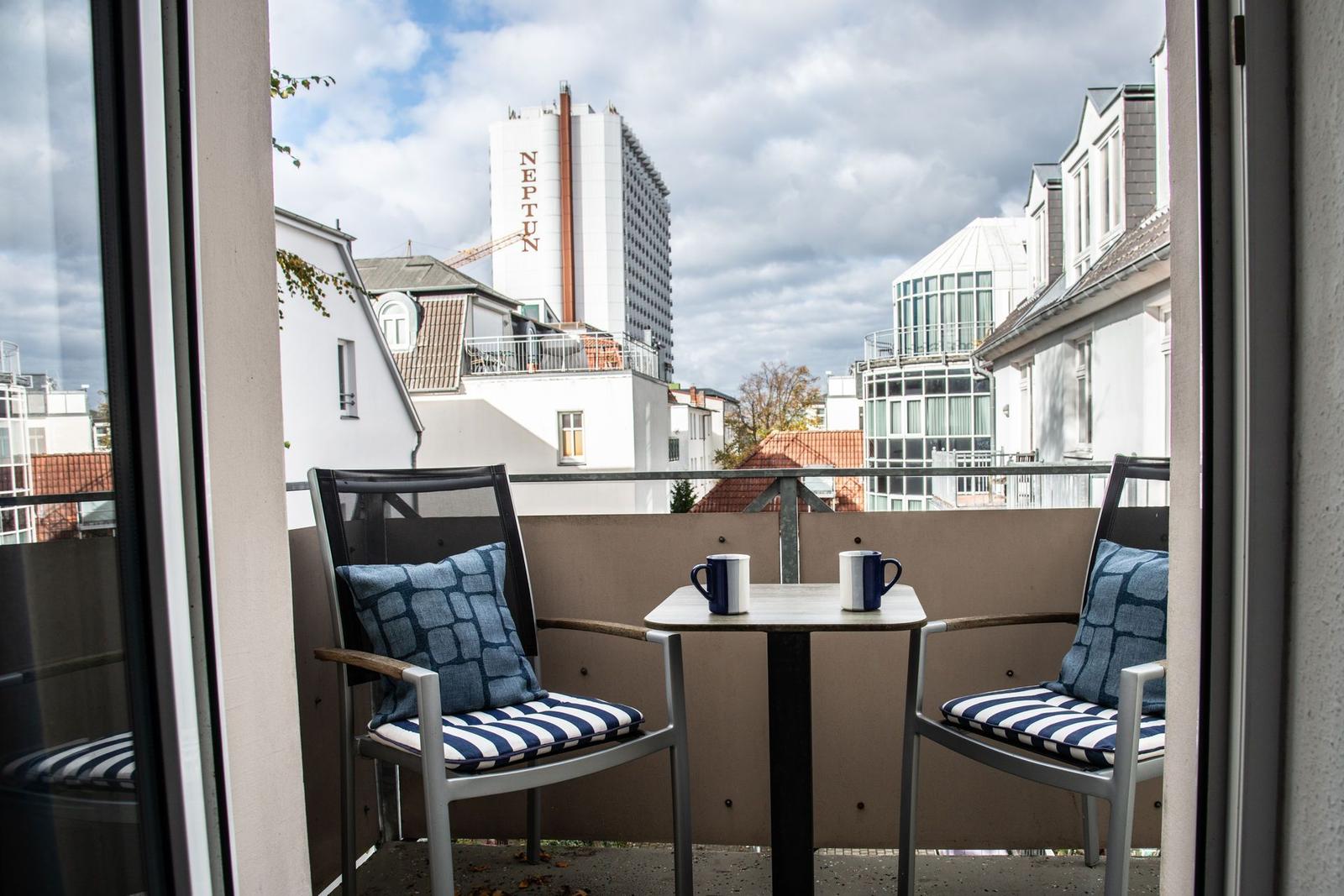Balcony with two chairs and table, overlooking city buildings including a tower with NEPTUN sign.