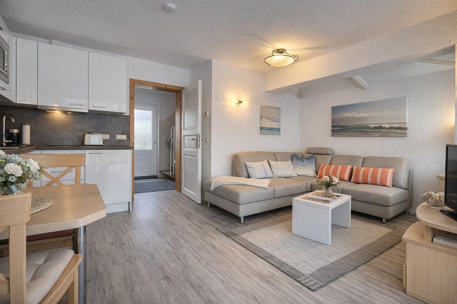 Wohnbereich mit Sofa, Couchtisch und Küchenbereich. Holzfußboden und Wandbilder.