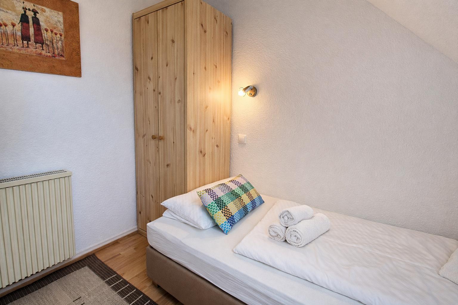 Ein Schlafzimmer mit Bett, Holzschrank und Wandbild. Drei Handtücher liegen auf dem Bett.