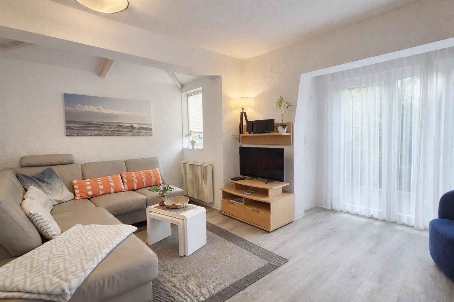 Wohnzimmer mit Sofa, Fernseher und Fenster mit weißen Vorhängen.