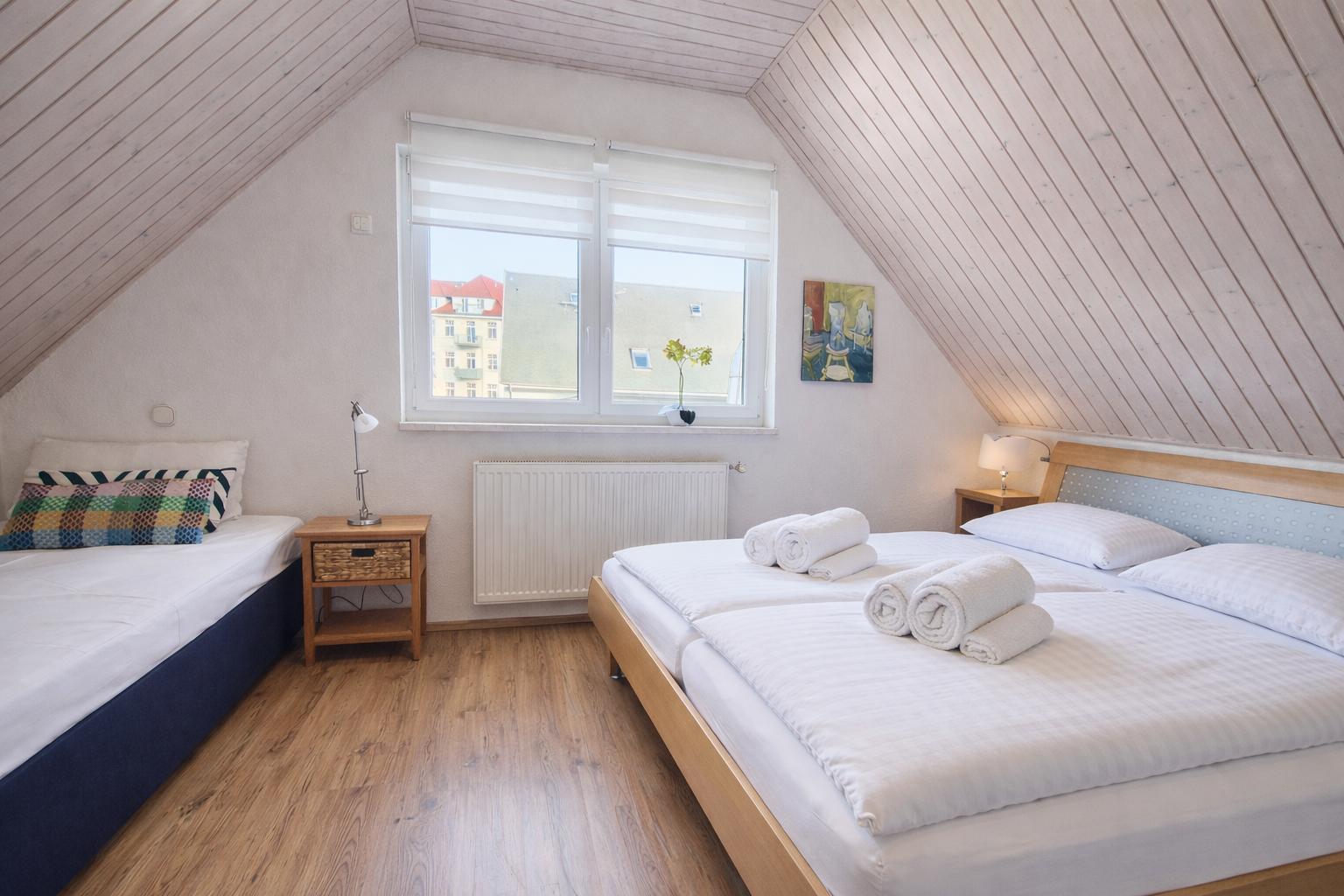 Zimmer mit Dachschrägen, zwei Betten, Fenster und Holzboden.