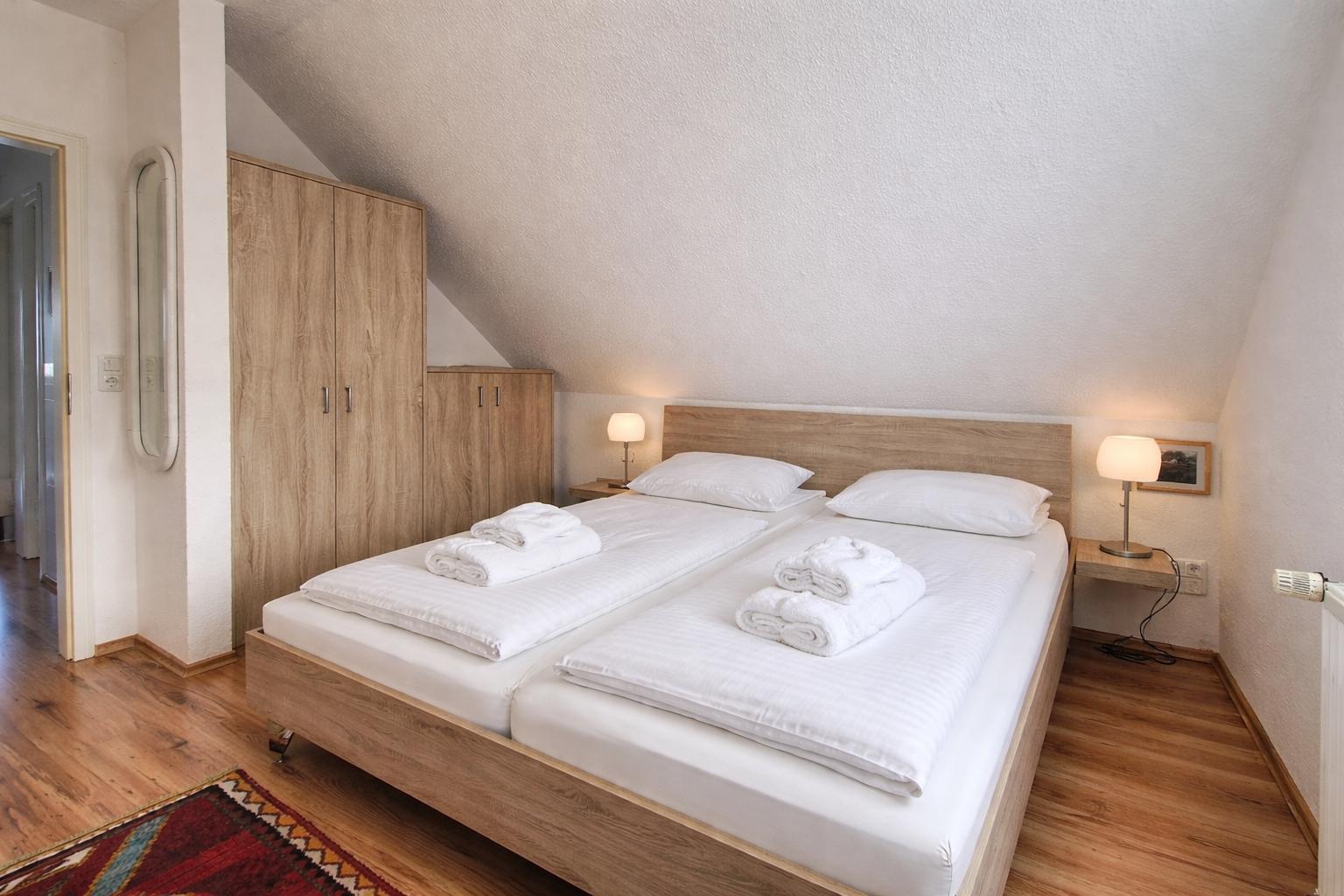 Schlafzimmer mit Doppelbett, Holzmöbel und Stehspiegel. Dachschrägen Decke und Holzboden.