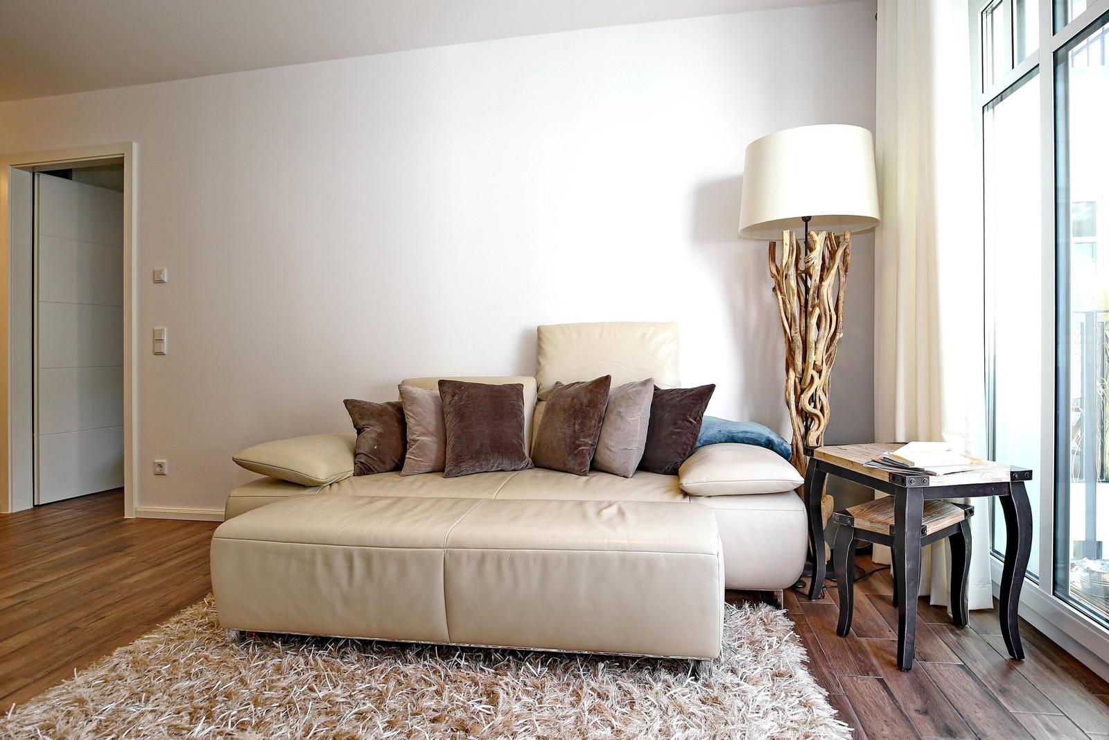 Ein Wohnzimmer mit einem hellen Sofa, Kissen und einer Stehlampe neben einem Fenster.