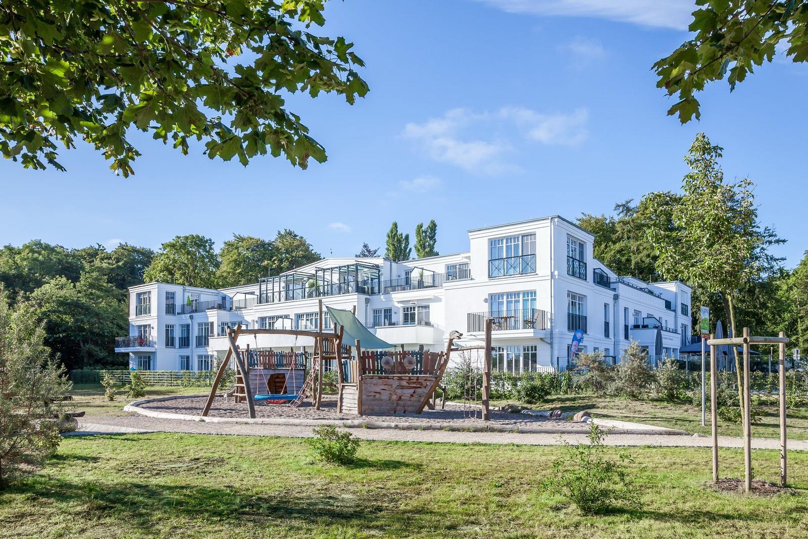 Weiße Ferienwohnung mit Spielplatz und Grünanlagen im Hintergrund.