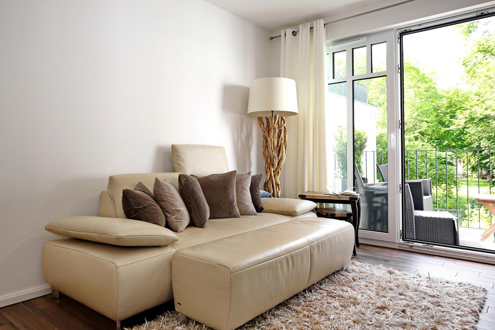 Ein Wohnzimmer mit cremefarbenem Sofa, dekorativen Kissen und einer Terrasse mit Blick auf Grünflächen.