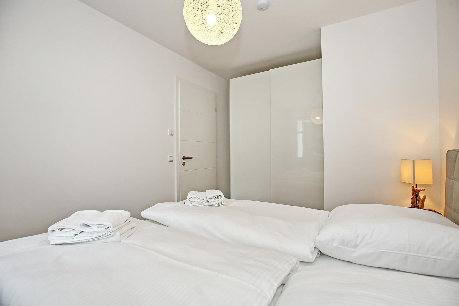 Schlafzimmer mit weißem Bett, KleiderSchrank und Lampe.