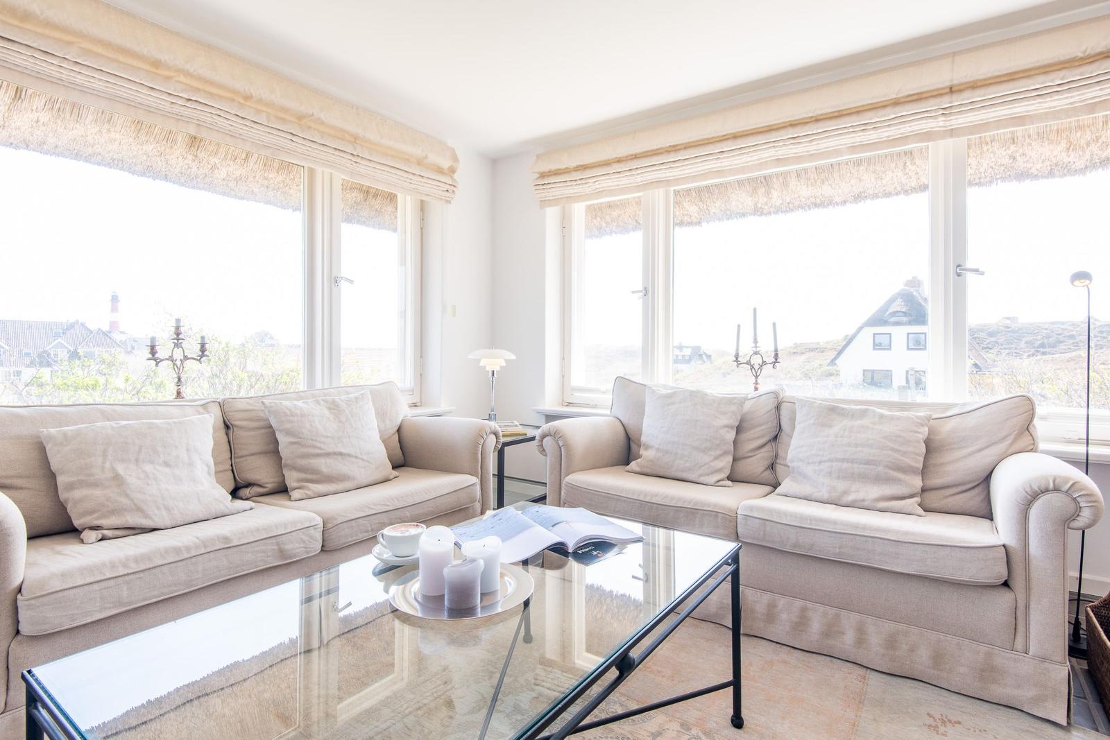 Two sofas with cushions are positioned in front of large windows with a view of the landscape.