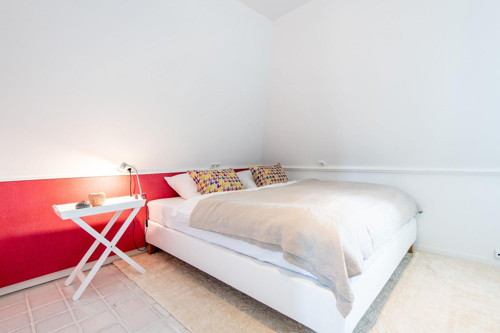 Bedroom with white bed, red wall, and small table.