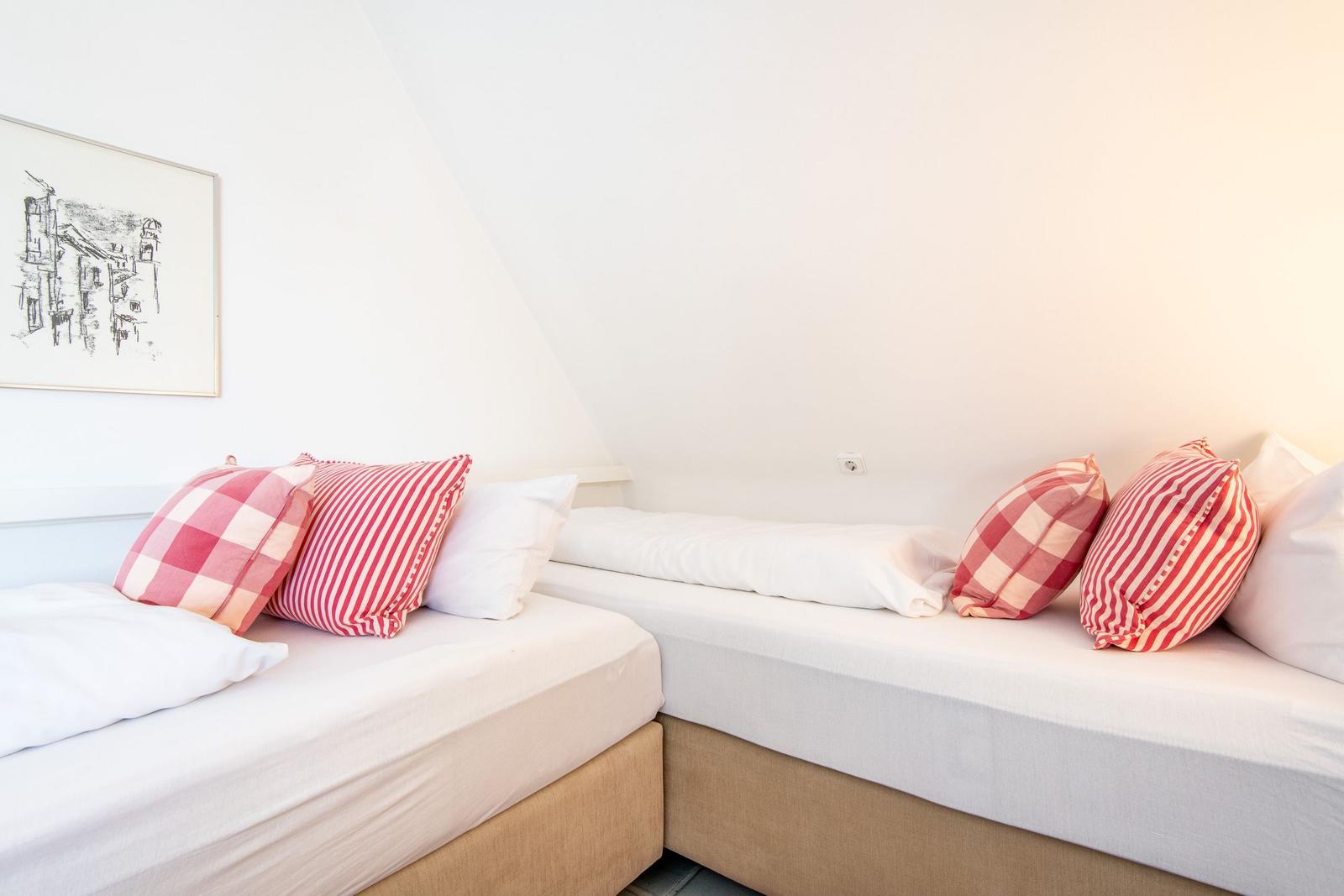 Two beds with white sheets and red pillows under sloped walls.