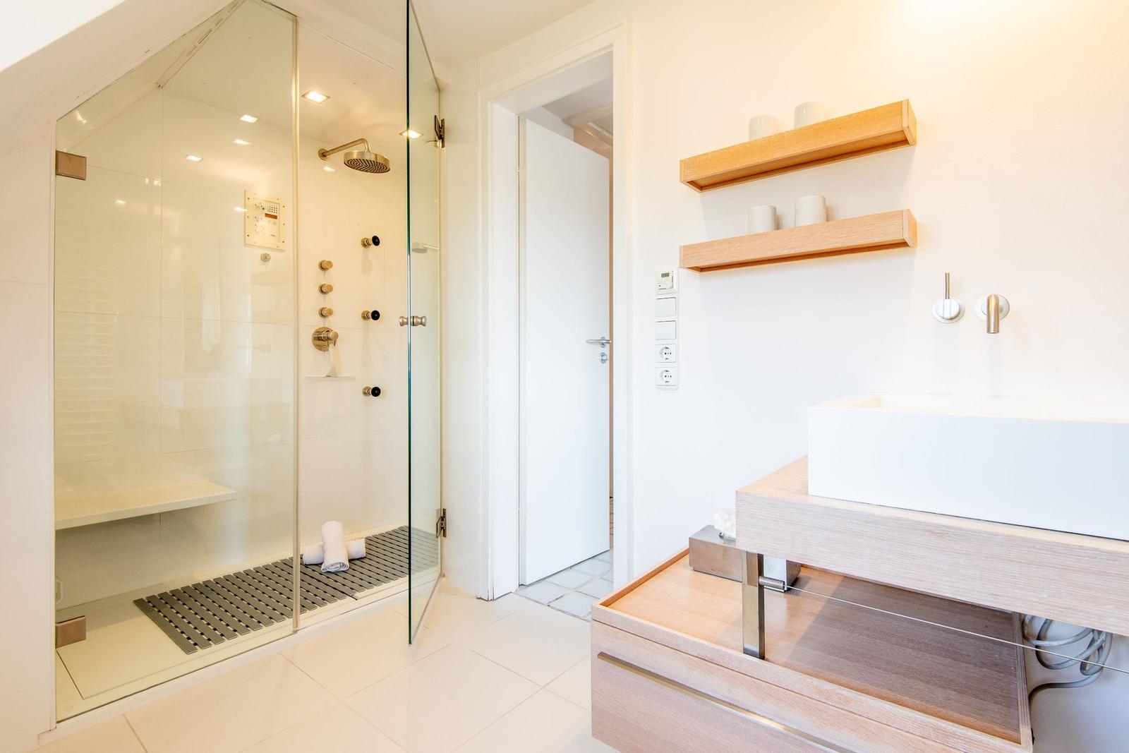 Shower with glass enclosure, sink, and wooden shelves on the wall.