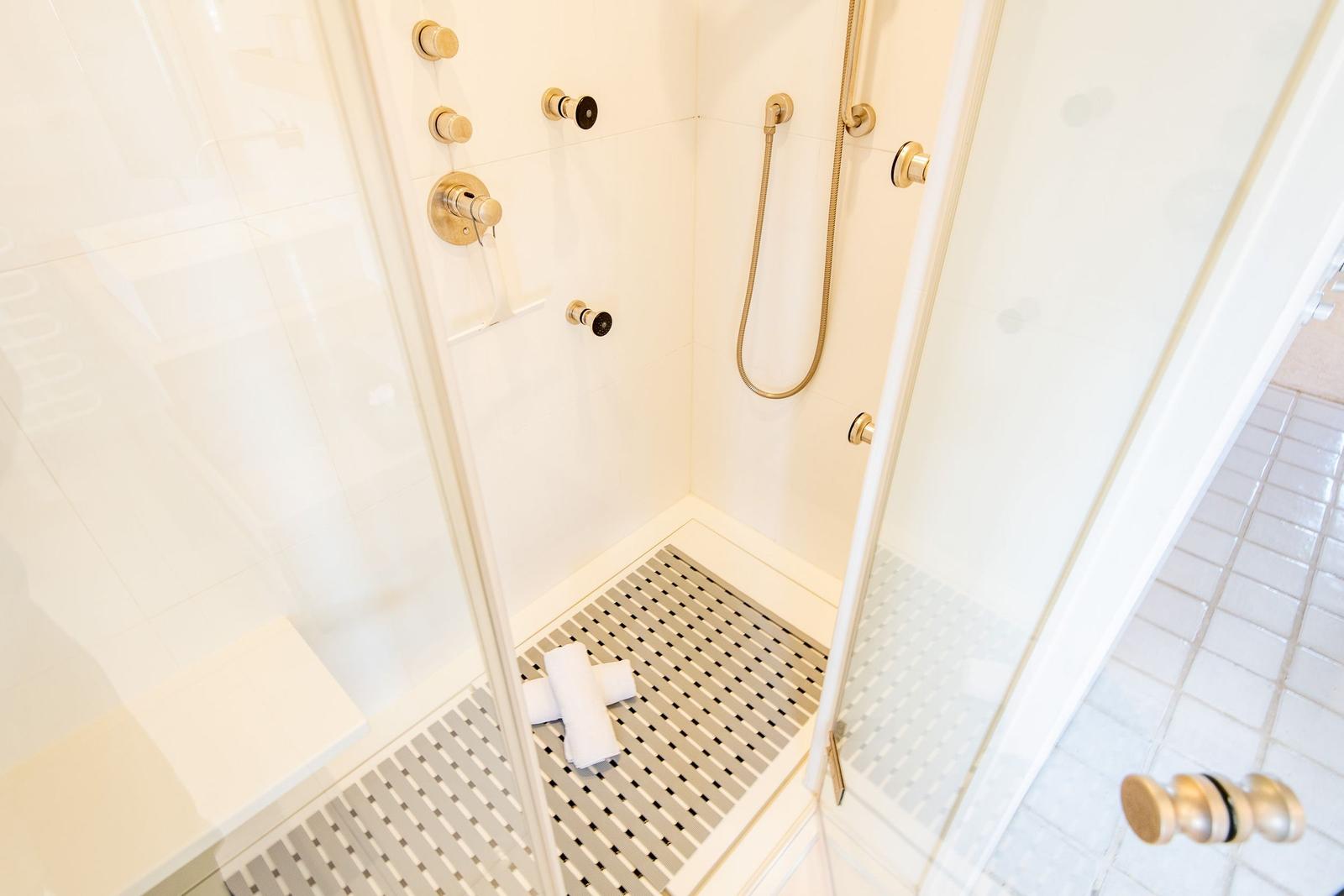 Shower with glass door, gold handles, and tiled floor.