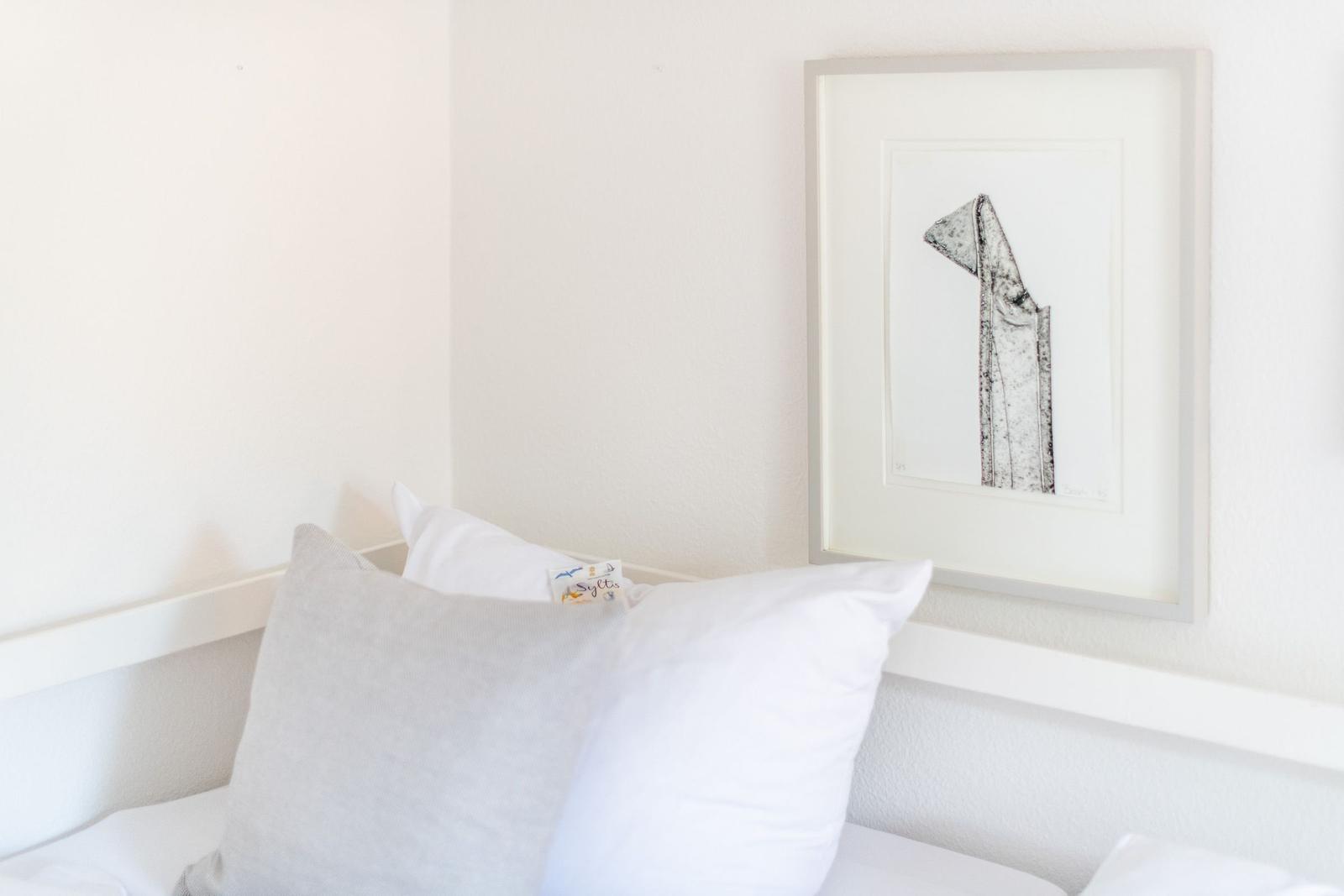 Bed headboard with pillows and framed drawing on the wall