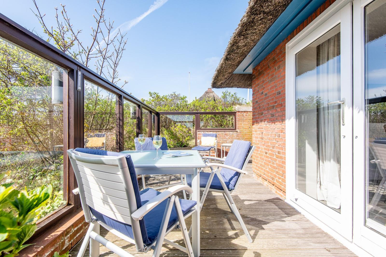 Terrace with table and chairs, view of greenery and house wall.