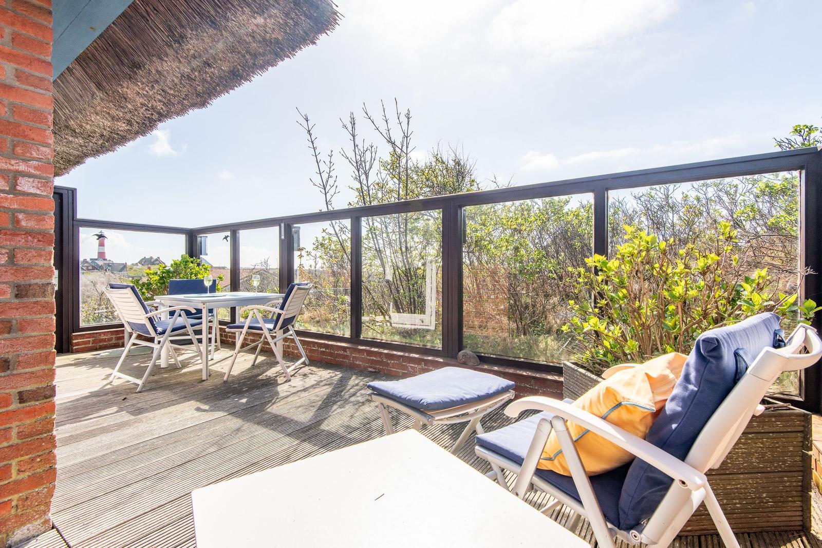 Terrace with table, chairs, and seating. View of greenery and lighthouse.