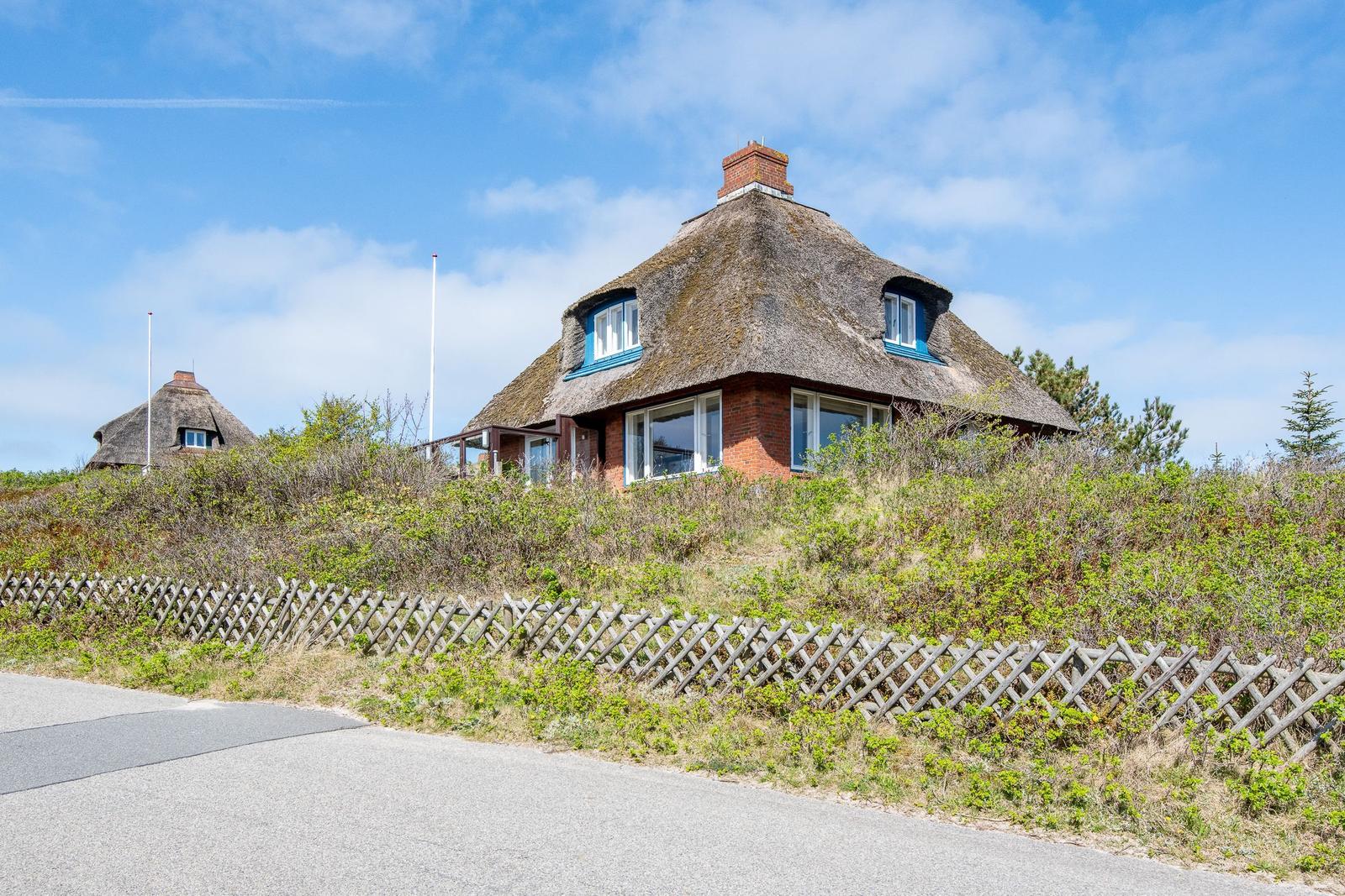 Cottage with thatched roof and wooden fence beside a road.