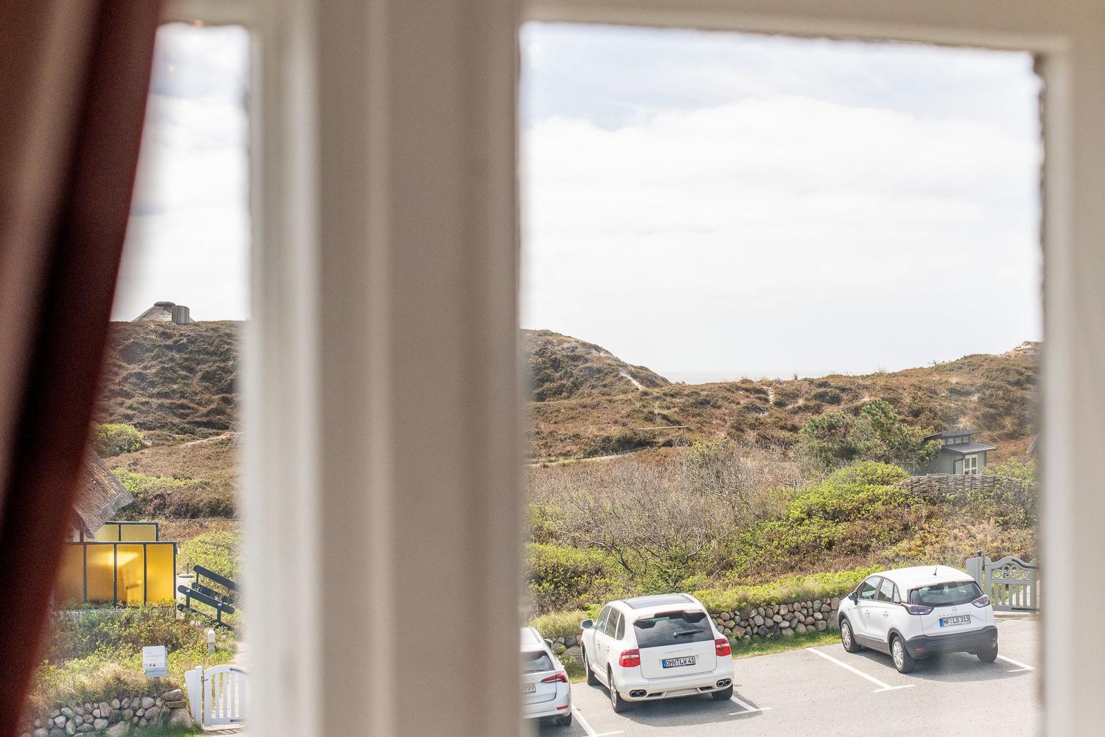 View through window onto parking lot with cars and hillside landscape.