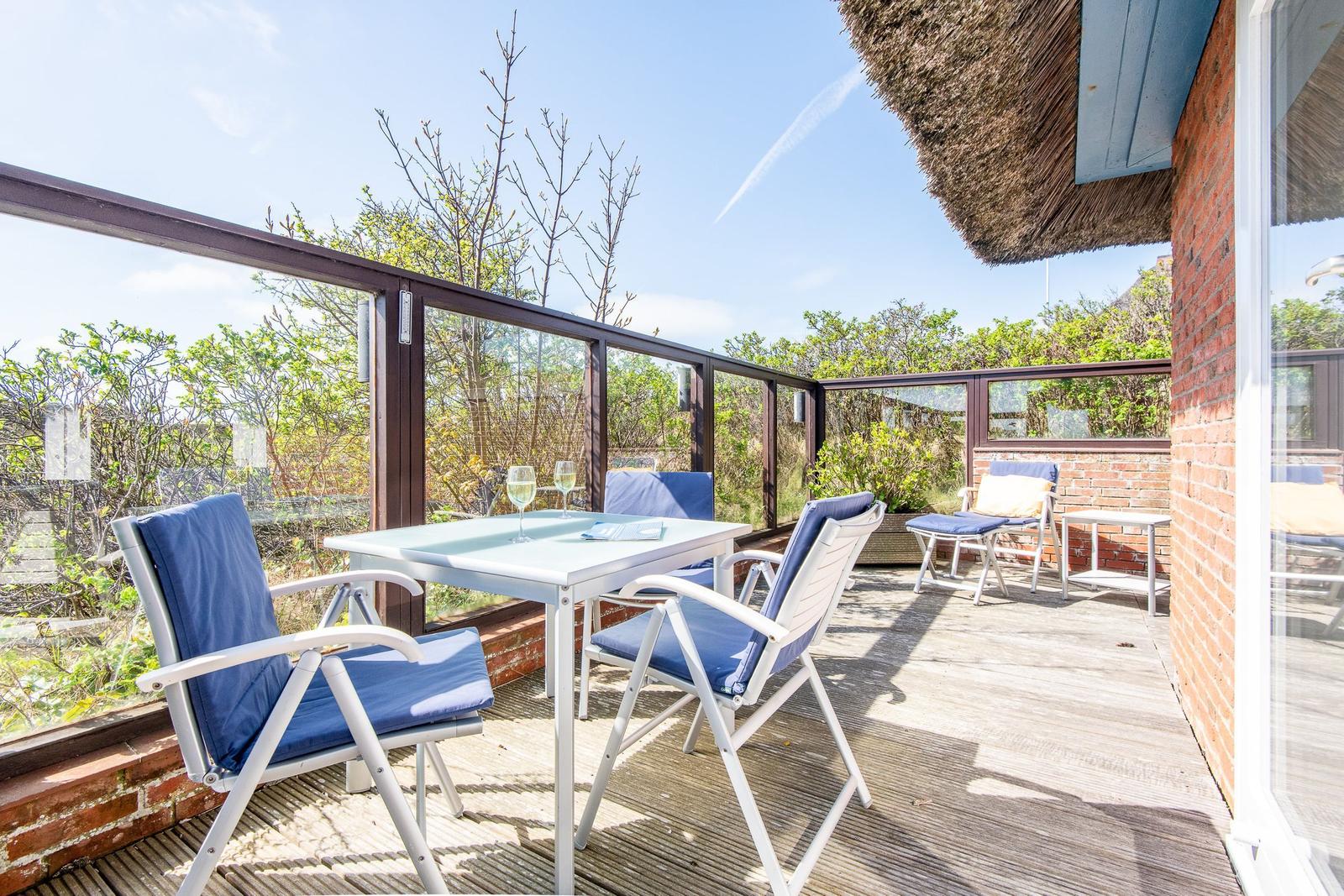 Terrace with table and chairs, glass wall and thatched roof.
