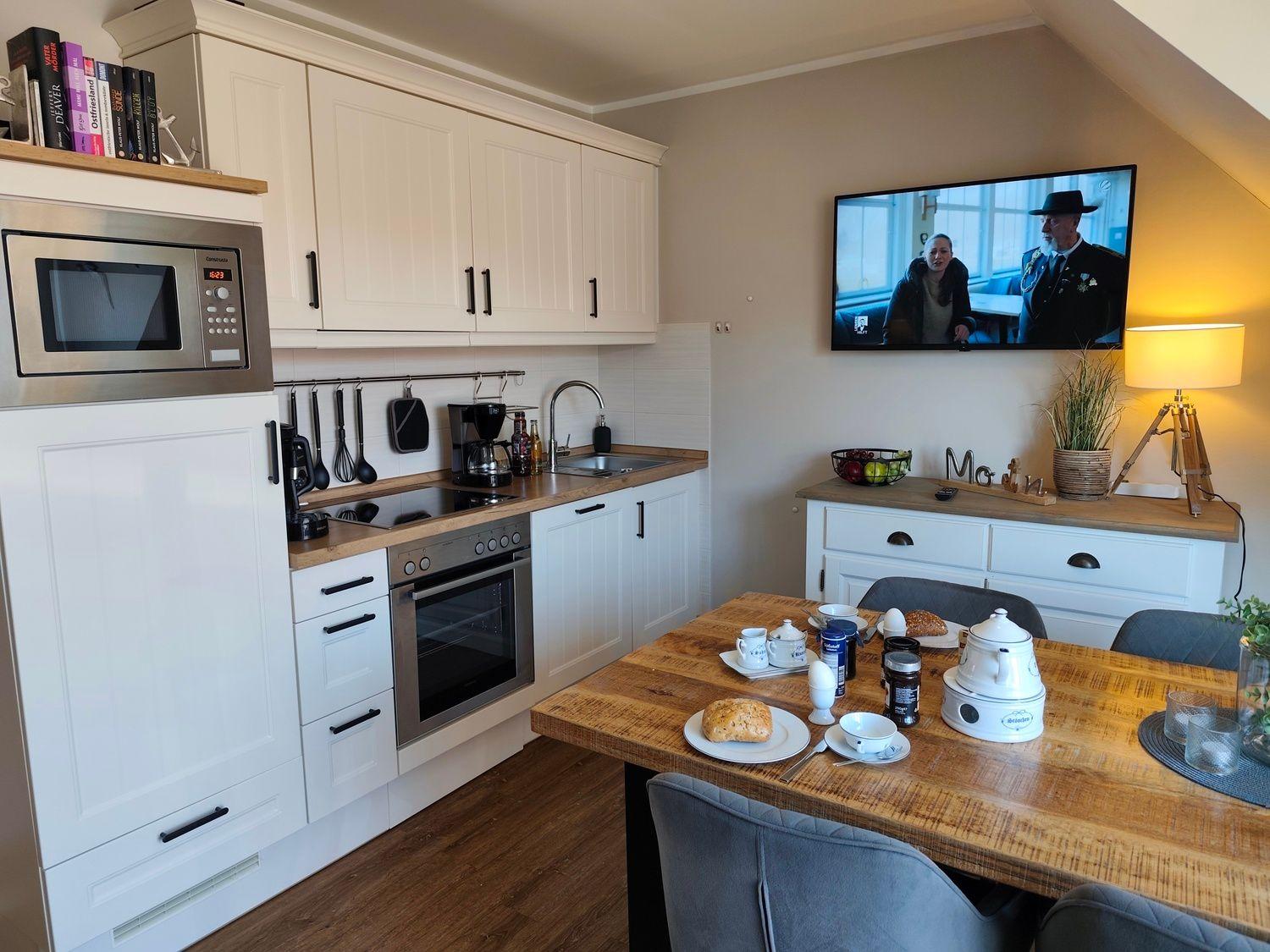 Küche mit Essbereich, Fernseher und Holztisch mit Frühstück.
