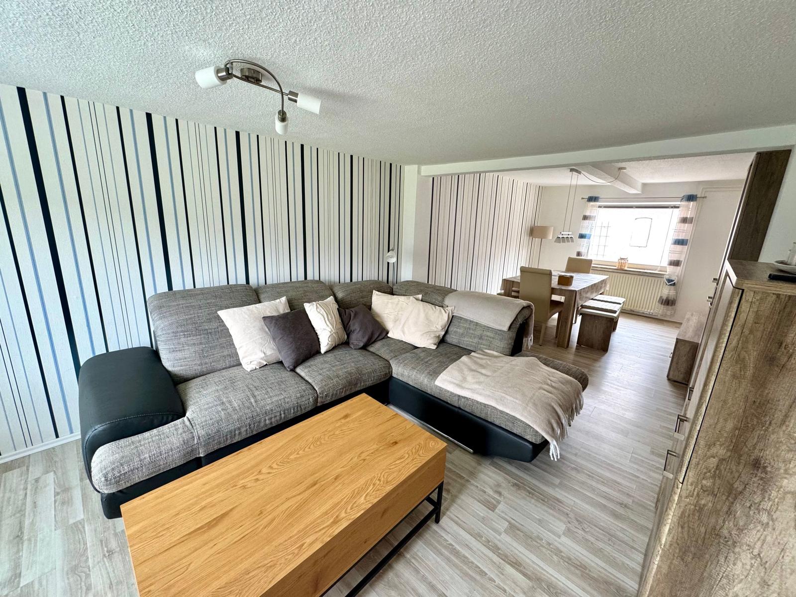 Wohnzimmer mit Sofa, Couchtisch und Essbereich im Hintergrund.