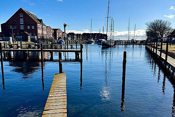 Hafen mit Booten und hölzernen Stegen unter blauem Himmel.